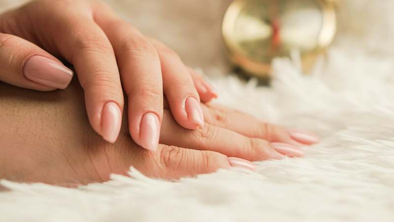 Close-up of elegant hands holding various professional nail files against a soft neutral backdrop